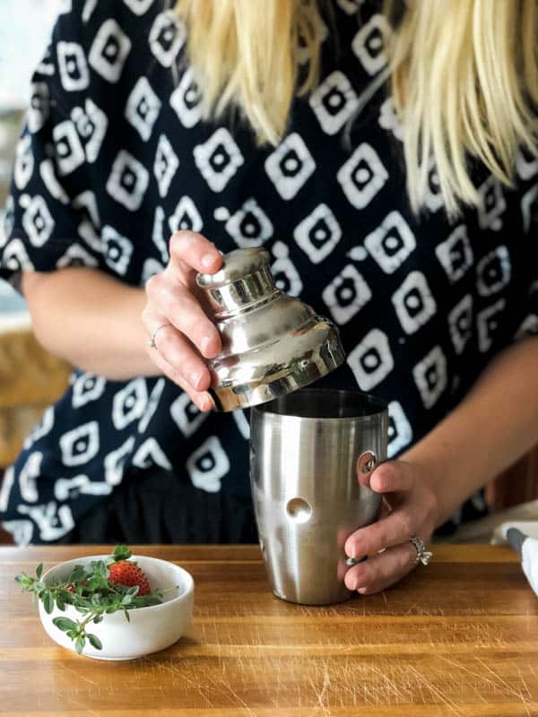 Woman adding a lid to a cocktail shaker. 