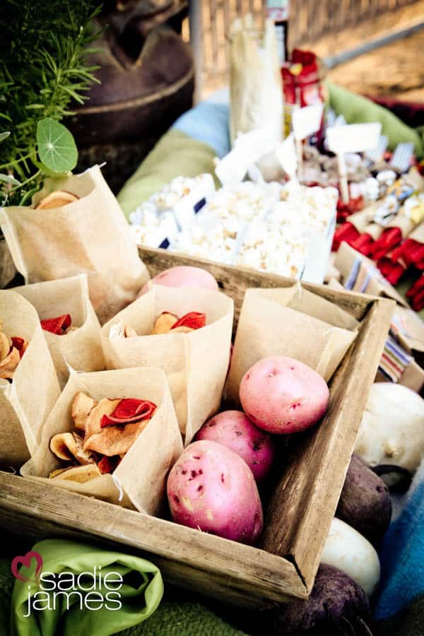 Outdoor movie night food display with potato chips and potatoes in a wooden box with more snacks in the background.