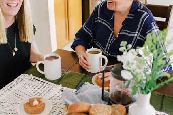 Two women enjoying a cup of cinnamon spiced coffee at a table. 