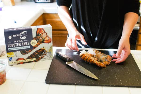 Woman cutting lobster tails on a cutting board.