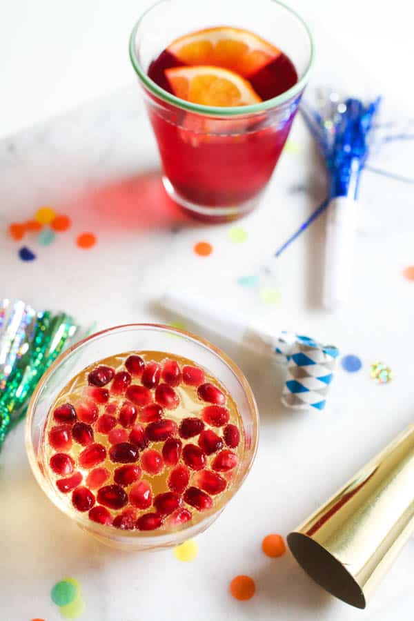 Top down, close up image of new years non alcoholic drinks surrounded by noisemakers and confetti.
