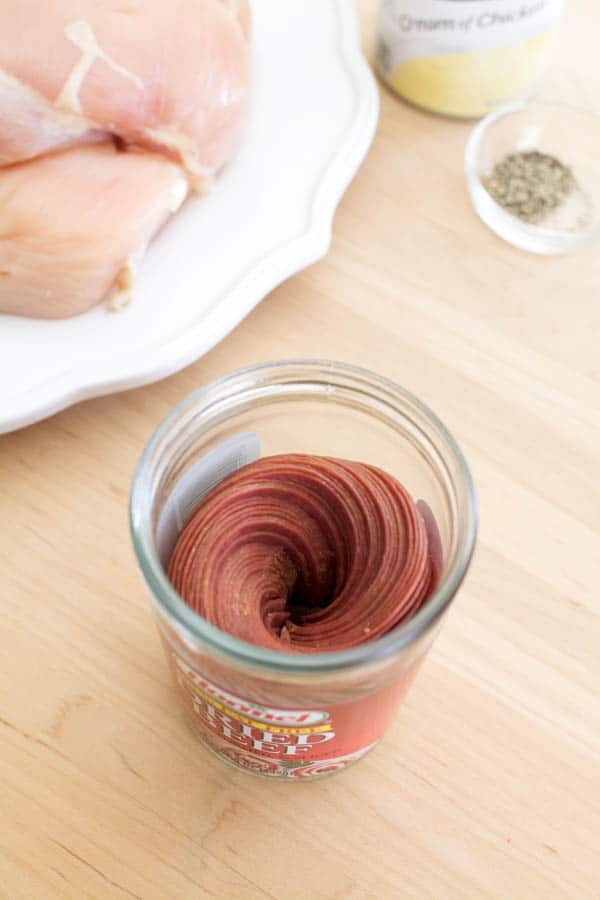 Dried beef in a jar on a counter next to a plate of raw chicken. 