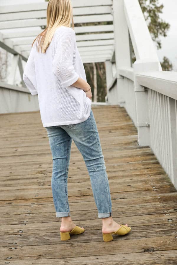 Woman in jeans and white top with lime green mules on a bridge. 