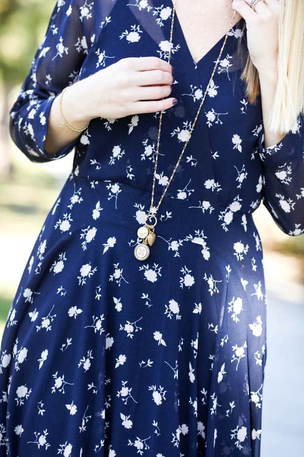 Close up of a long necklace on a women in a blue floral dress. 