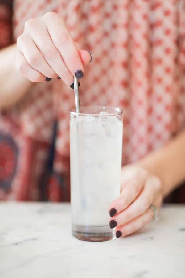 Woman stirring a cocktail on a counter with a long bar spoon. 