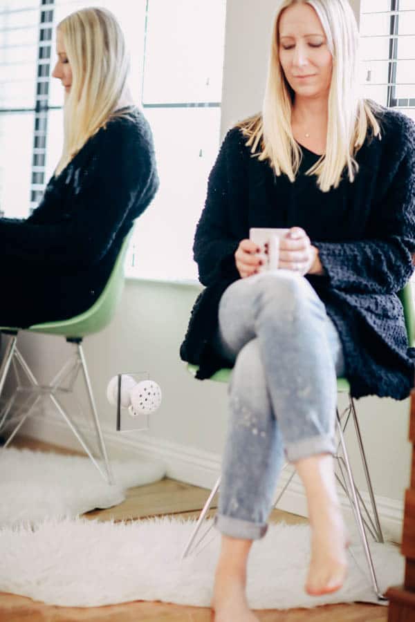 A woman sitting in a char holding a mug next to a plug in essential oil diffuser in the outlet. 