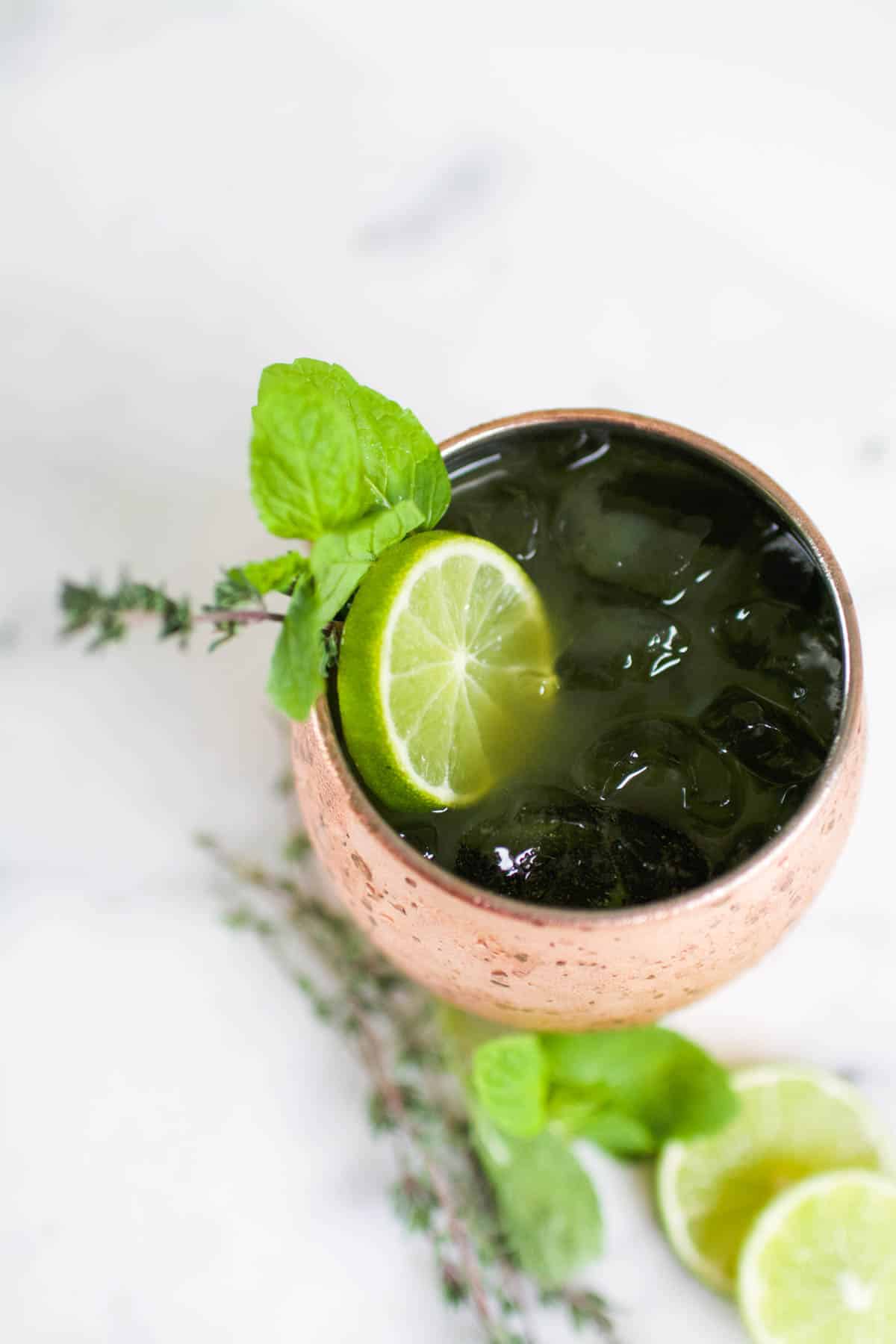 Top down view of a copper Moscow Mule mug holding a green cocktail and garnished with a lime slice and fresh herbs for St. Patrick's Day.