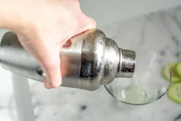 Girl pouring drink into a stemless martini glass from a cocktail shaker.