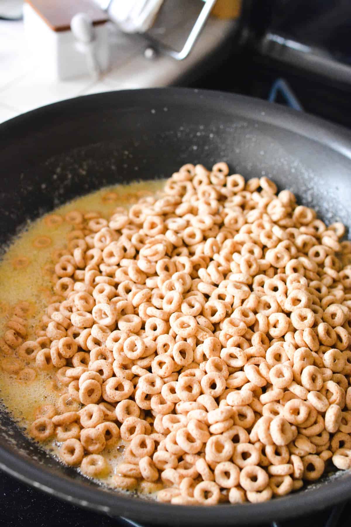 Cheerios in melted butter in a pan on the stove.