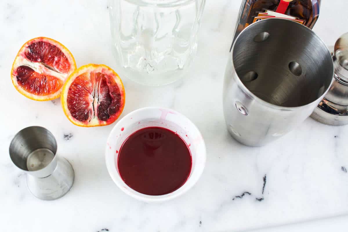 Fresh squeezed blood orange juice in a small white bowl next to a cocktail shaker.