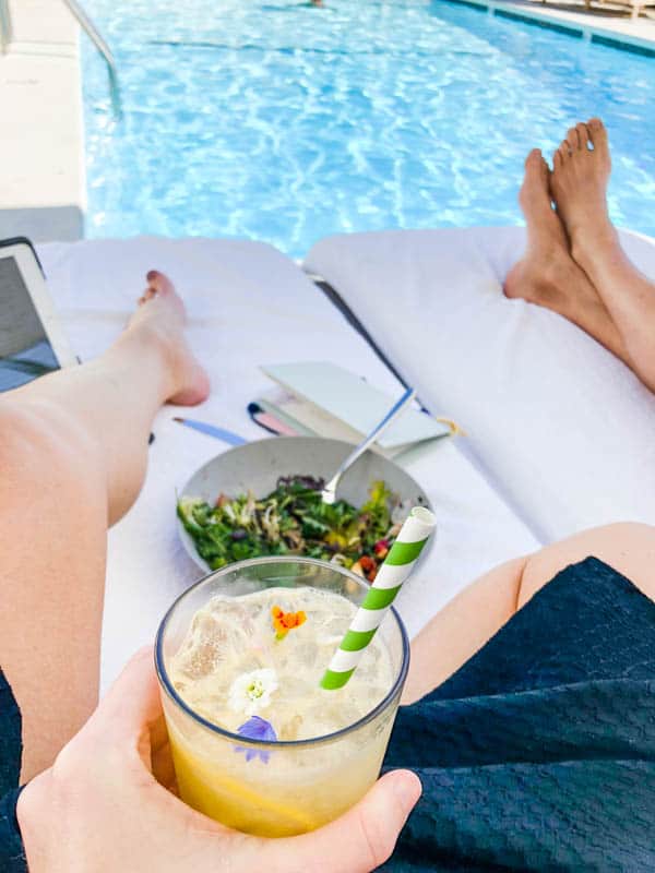 Girl's hand holding a cocktail by the pool while eating lunch.