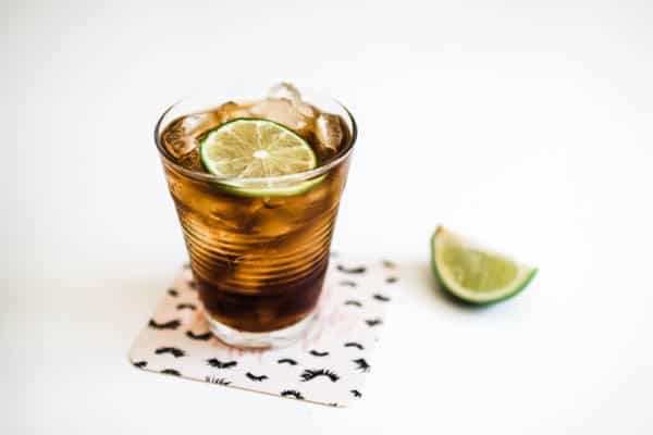 Glass of coke on a coaster on a table with a lime wedge next to it.