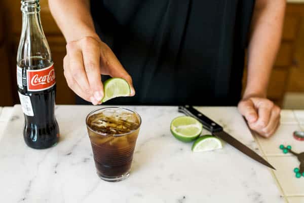 woman squeezing lime into a glass of coke on a cutting board