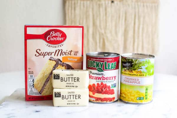 Ingredients for making a strawberry dump cake sitting on a marble cutting board.