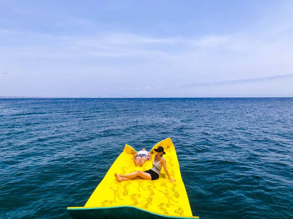 2 women sitting on a lily pad float in the Pacific ocean.