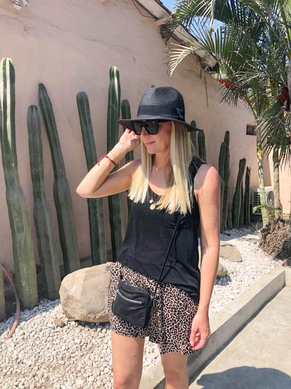 girl in black hat and leopard print shorts in front of a wall of cacuts.