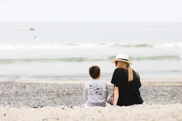 mom and son sitting facing the ocean on a beach