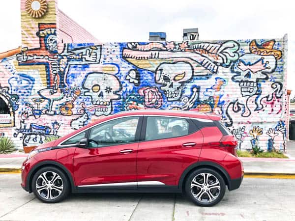 Red Chevy Bolt electric car in front of graffiti wall.