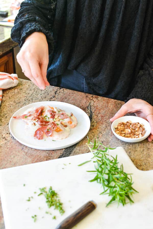 Girl adding chopped nuts to a pasta dish.