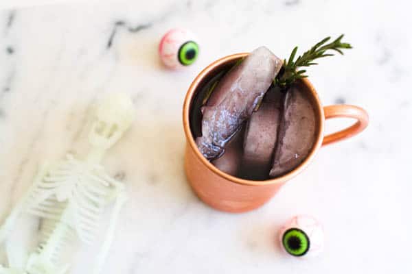 A copper Moscow Mule mug with a black cocktail in it on a marble table next to some Halloween decorations.