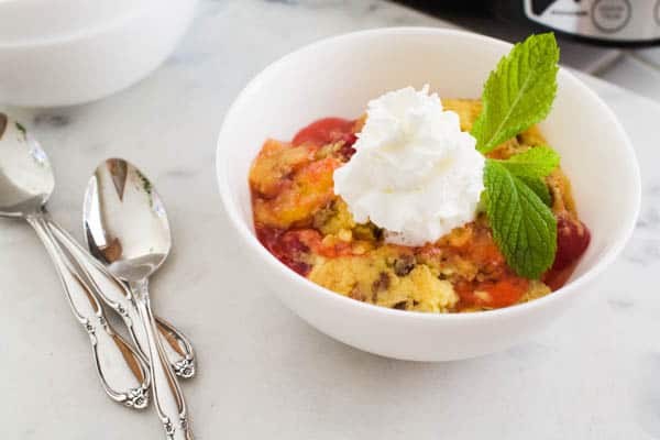 Apple cherry dump cake in a bowl next to a crockpot.