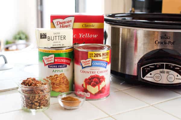 Ingredients to make an apple cherry dump cake on the counter next to a crock pot.