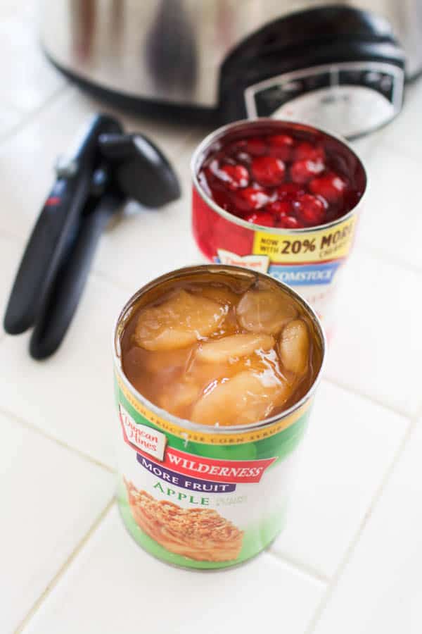 Cans of cherry and apple pie filling next to a crock pot for a dump cake.