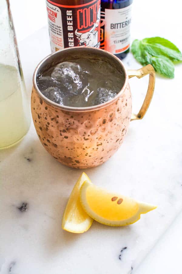 Overhead view of a copper Moscow Mule mug filled with ice and lemon wedges sitting on the table next to it.