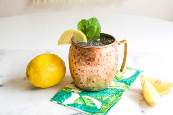 Moscow Mule cocktail in a copper mug on a table next to a lemon and lemon wedges.