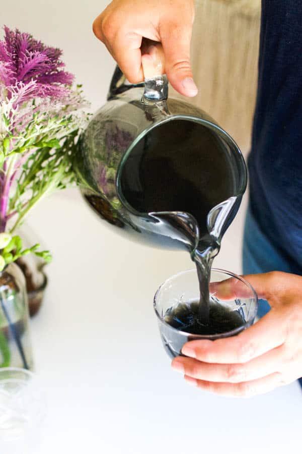 Woman pouring black Halloween punch with vodka into a punch glass.