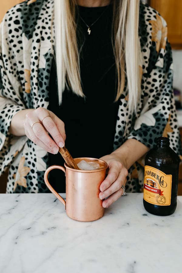 Woman adding a cinnamon stick as garnish to a fall mule.