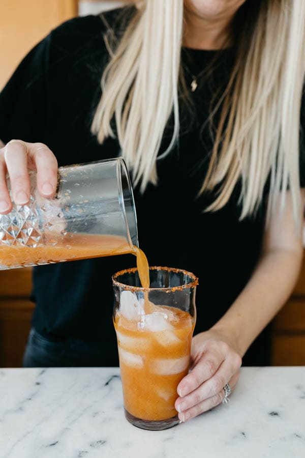 Pouring a Pumpkin Michelada with Estrella Jalisco into a glass with Tajin rim.