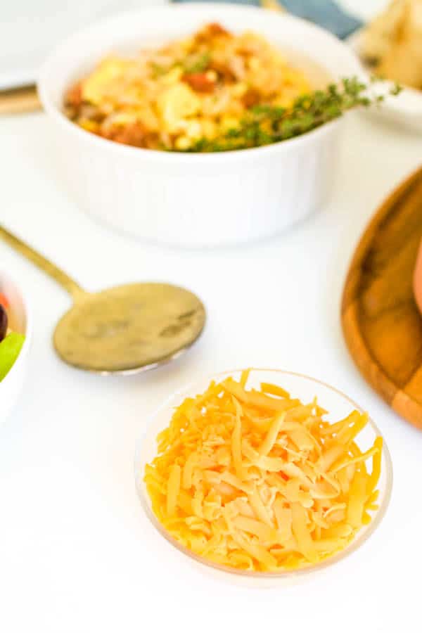 A bowl of cheese on a table next to a serving spoon