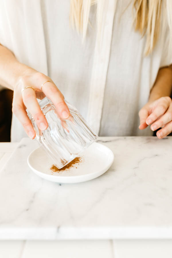 Woman dipping a rim of a cocktail glass into pumpkin pie spice on a plate. 