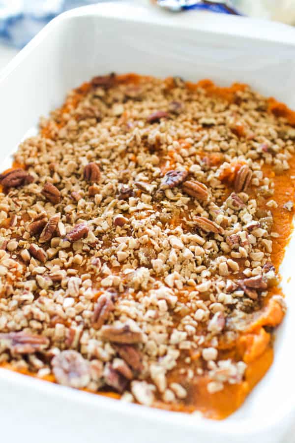 A unbaked pumpkin dump cake in a white baking dish topped with pecans and toffee bits.