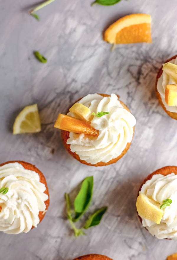 Frosted sangria cupcakes on a table with fruit and herbs.