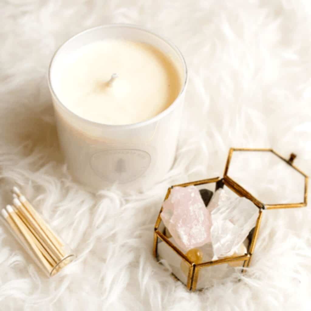 Close up of a candle and quartz crystals in a small box on a white furry rug.