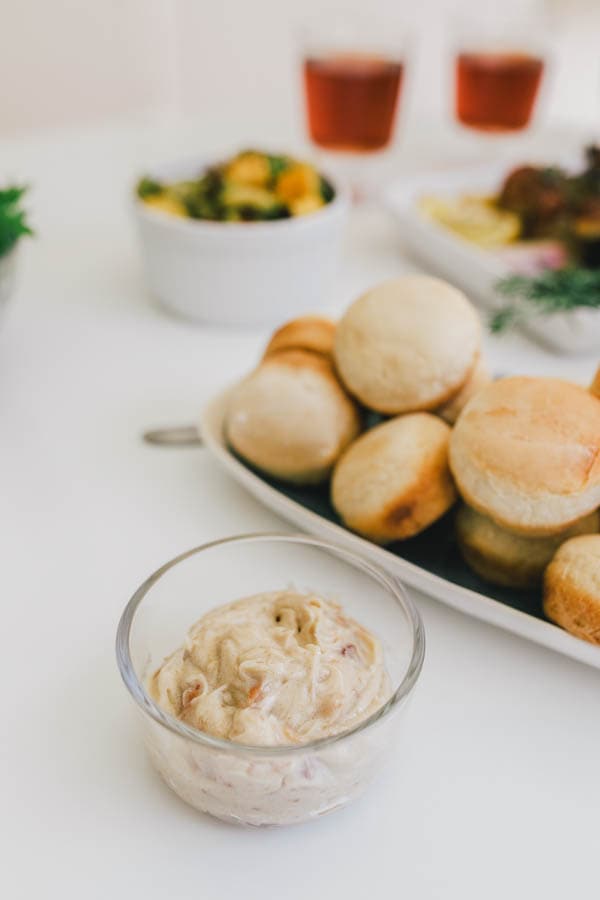 Bacon compound butter with brown sugar and vanilla in a small glass serving dish next to a platter of rolls.