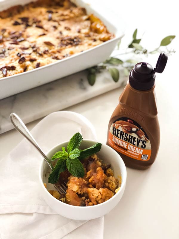 Sweet potato dump cake in a bowl next to caramel syrup on a table. 