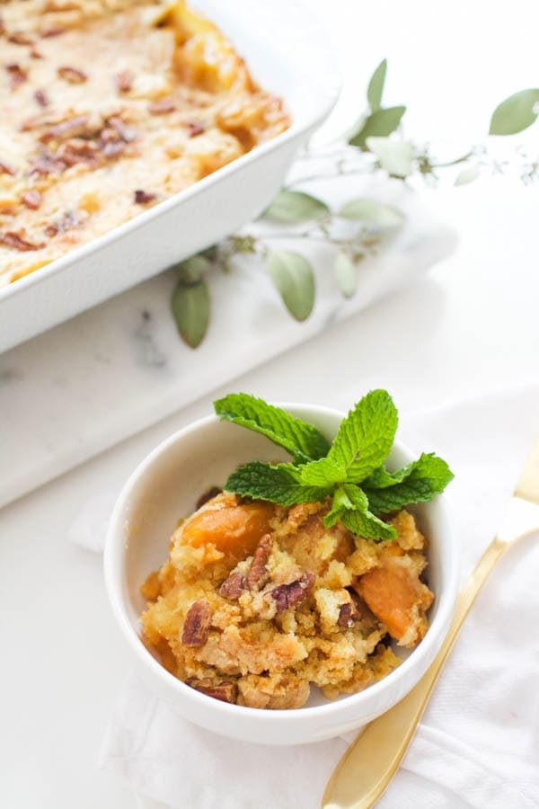 Small white serving bowl with a portion of Sweet Potato Dump Cake on a table with a mint garnish. 