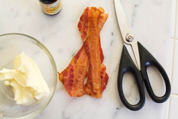 Softened butter and cooked bacon on a cutting board for a compound butter recipe.