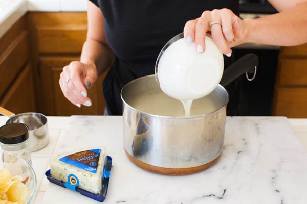 Add heavy cream to a pan to make a blue cheese sauce for potato chip nachos.