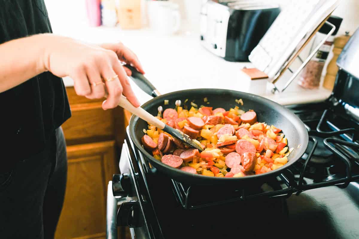 Woman cooking sausage and peppers on the stove.