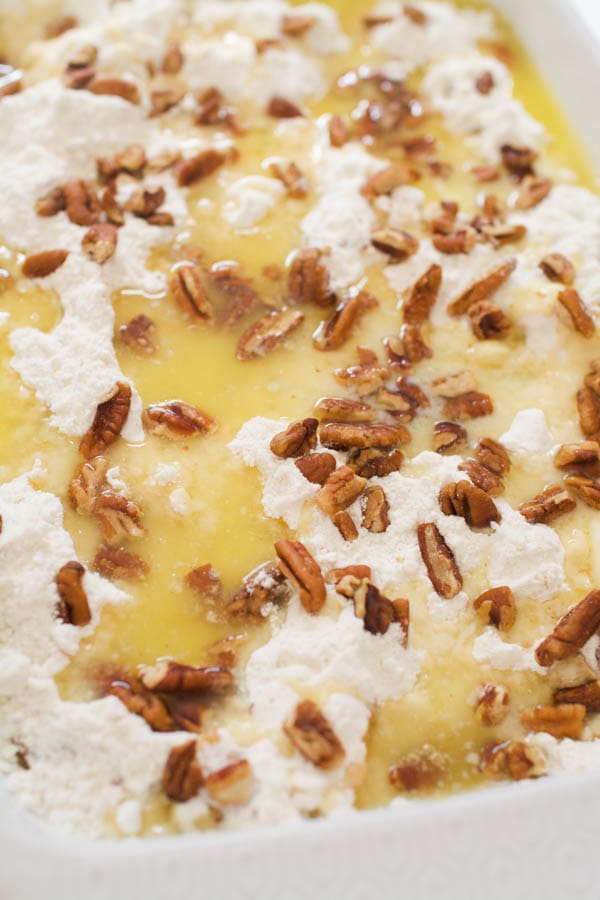 Melted butter and pecans on top of dry cake mix for a dump cake in a baking dish. 