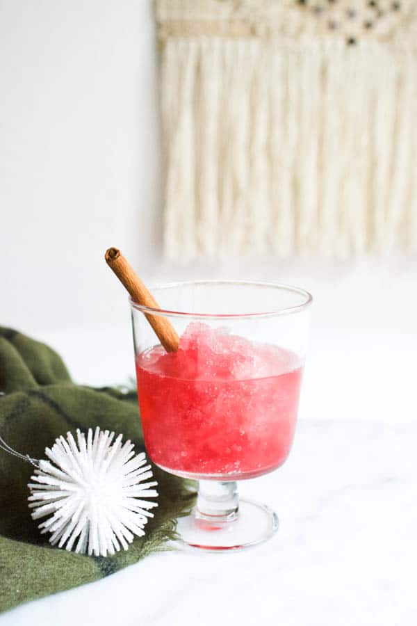 Cranberry Vodka Slush cocktail in a glass on a table next to an ornament. 