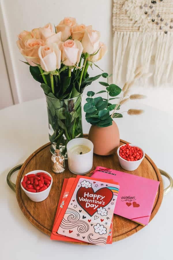 Wood tray topped with vases of fresh flowers, small bowls of candy, candles and greeting cards.