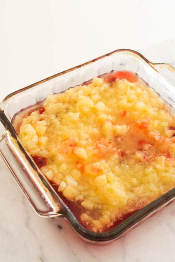 A small glass baking dish with cherry pie filling and crushed pineapple for a dump cake.