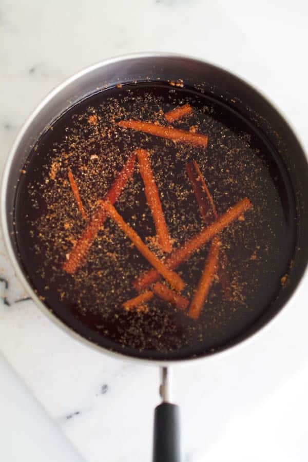 Spiced and cinnamon sticks infusing cranberry juice in a pan.