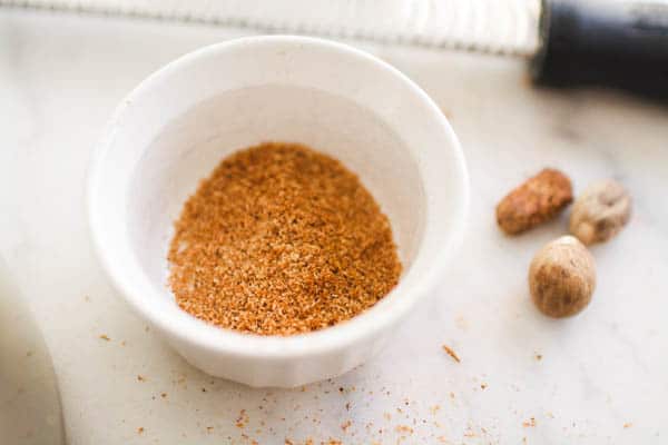 Fresh nutmeg in a small bowl on a cutting board.