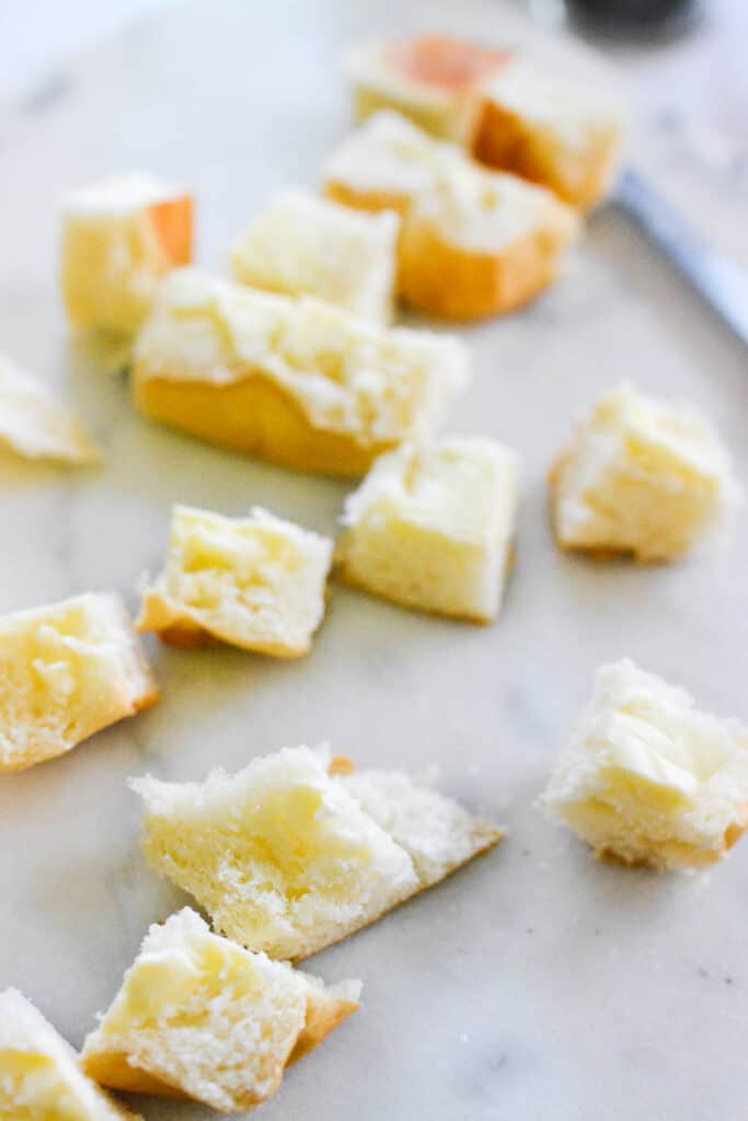 Hawaiian rolls cut into chunks and buttered laying on a cutting board.